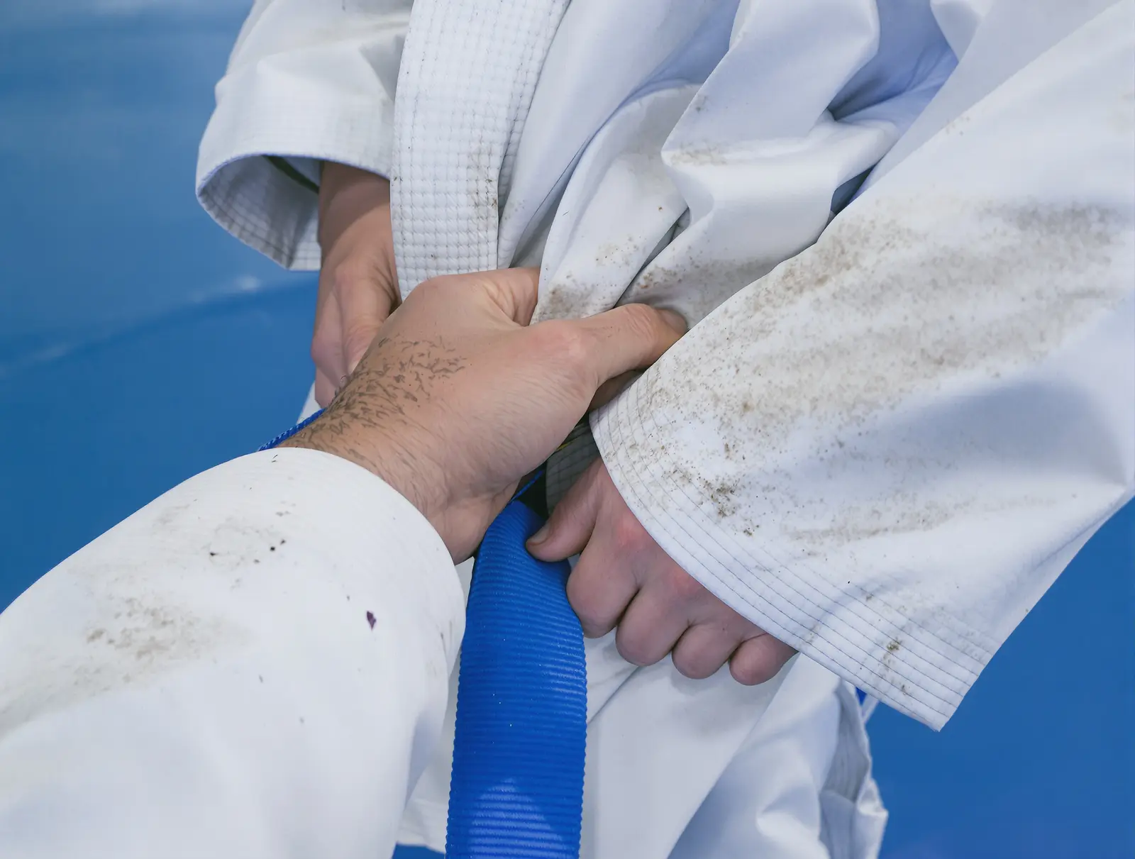 Close-up of a hand gripping the collar of a white gi above a blue belt