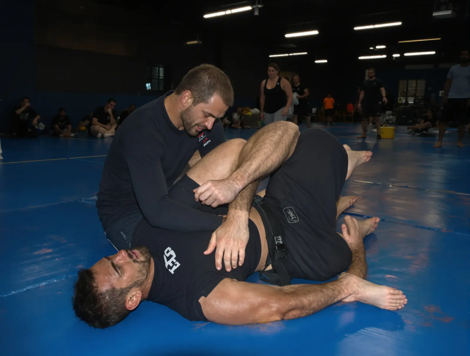 Two men in rash guards training no-gi jiu jitsu during an evening class